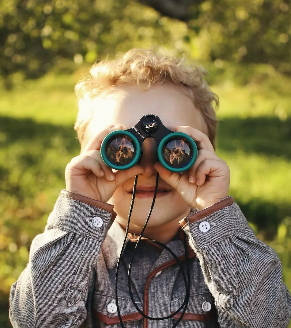 child standing while using green binoculars